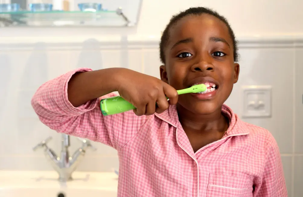 Young girl in pink pajamas brushing her teeth with a green tooth brush.