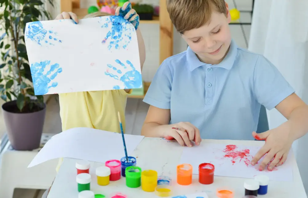 Two kids finger painting in a classroom setting.