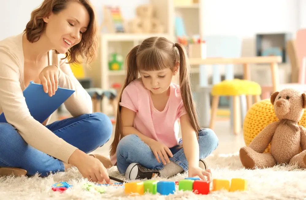 A teacher and student playing with blocks on the carpet.